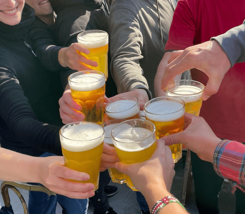Gruppe stößt mit Biergläsern an Bord eines Traditionsseglers an – gesellige Stimmung beim Mitsegeln.